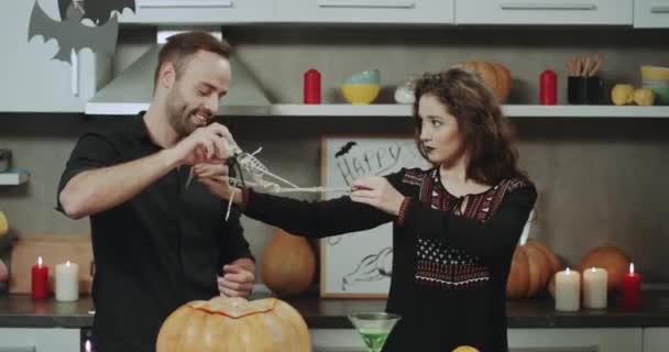 Casal carismático na noite de Halloween brincando com um esqueleto, ter um tempo engraçado juntos — Vídeo de Stock