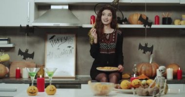 Komik ve güzel maskeli Cadı Cadılar Bayramı gecesi aperatifler için kamera düz seyir ile bir tabak tutarak mutfağa, iyi bir ruh hali var.