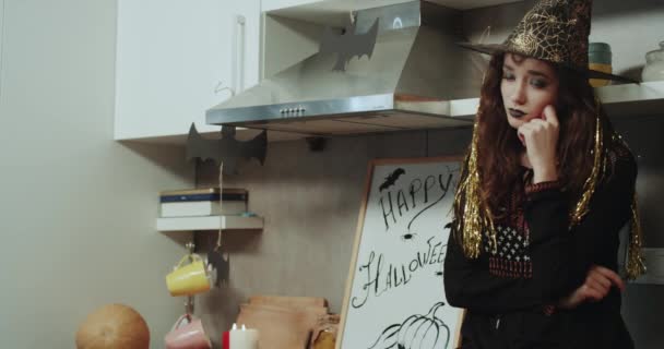 Una bruja con cara triste tiene mal humor en la noche de Halloween, sentada en la mesa de la cocina. 4k — Vídeos de Stock