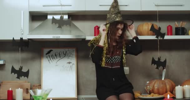 A curly hair witch dacing and moving charismatic in front of the camera she is sitting on the kitchen table. — Stock Video