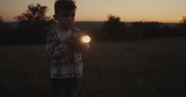 Geweldig uitziende jongen spelen met een zaklamp bij zonsondergang. — Stockvideo