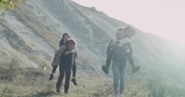 İki genç çift birlikte doğa onların sırtından arkadaşlarını tutarak ve alan gülümseyen ve iyi bir ruh hali ile yürüyen çocuklar eğlenmek.