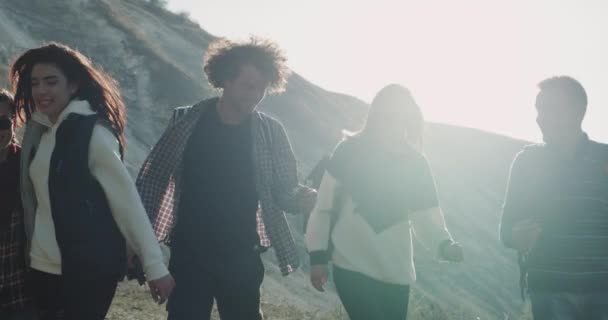 Een goed uitziende multiculturele jongeren lopen omarmen door het veld in het midden van de berg. — Stockvideo