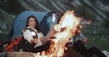 Kamp ateşi iki kadın ve bir adam bir harika birlikte, onlar bir şey bazı parlak havai fişek tutarak ve büyük onları tutan gülümseyerek kutluyor vakit.