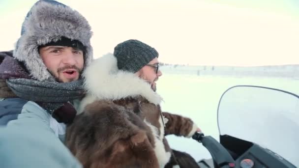 Dos tíos en medio del Ártico en tundra, felices haciendo selfie video yendo en una máquina de nieve, a través de la nieve . — Vídeos de Stock