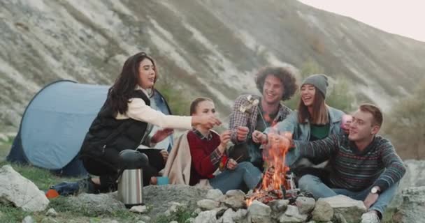 多种族的青少年有有趣的时间在旅行中, 吃棉花糖在篝火上燃烧. — 图库视频影像