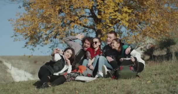 Selfie tijd voor een Instagram, grote groep multiculturele vrienden maken van foto's, op karakter naast is een grote kleurrijke boom. — Stockvideo