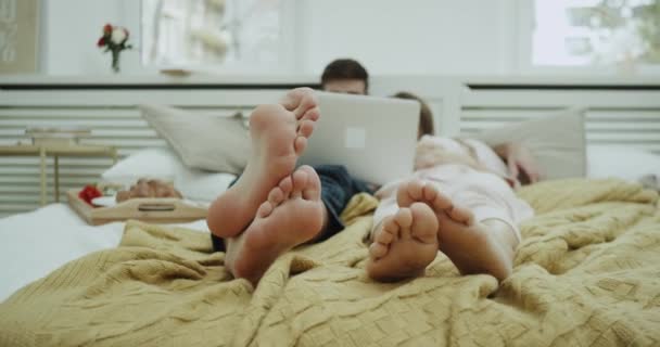 En el dormitorio una linda pareja pasando un rato romántico juntos viendo algo de notebook después de un delicioso desayuno . — Vídeos de Stock