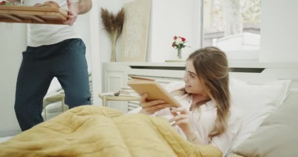 In the morning lady reading a book and waiting for her breakfast in bed from her boyfriend, they happy starting take the and feeling happy. выстрел по красному эпосу . — стоковое видео