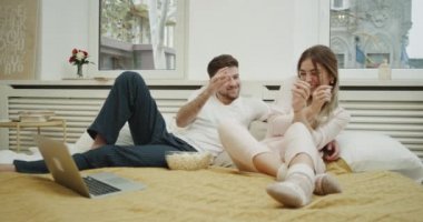 Güzel genç bayan ve onun ortağı pijama patlamış mısır yemek ve film seyrederken yatakta günler.