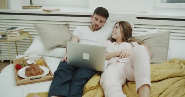 Un bon moment ensemble couple passant dans un appartement moderne dans leur chambre confortable ont une journée de lit regarder quelque chose sur le portable . — Video