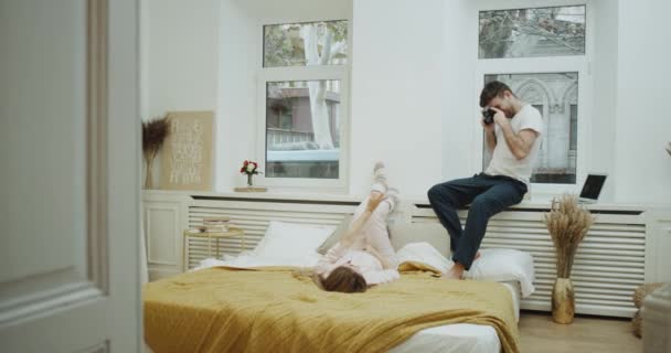 Amazing cozy design in bedroom , one couple have a romantic time together , man make some pictures for the lady they are both in pajamas. — Stock Video