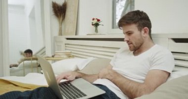 Rahat bir yatakta çalışma ile bir dizüstü bilgisayar, seyir karizmatik genç adam. 4k. Kırmızı epic vurdu