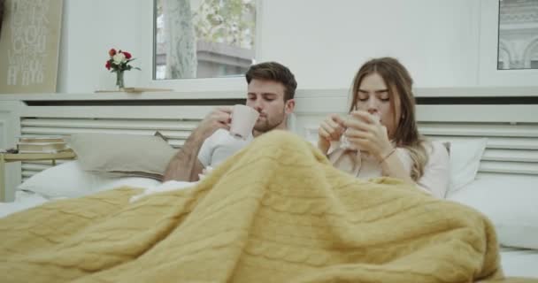 Couple in pajamas laying down on bed have a flu , coughing and feeling not good at all , drinking something warm. — Stock Video