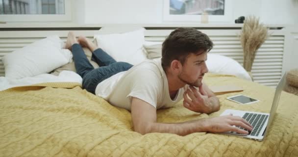У сучасній спальні чоловік в ліжку працює в своєму записнику дуже зосереджений . — стокове відео