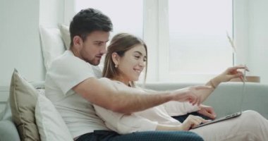 Kadın ve erkek portre onlar pijama giymiş modern bir oturma odasında kanepede otururken bir şey, sipariş için bir dizüstü bilgisayar kullanarak.