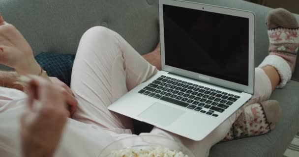 Detalhes de close-up do casal comendo pipocas no sofá e assistindo a um filme do caderno . — Vídeo de Stock