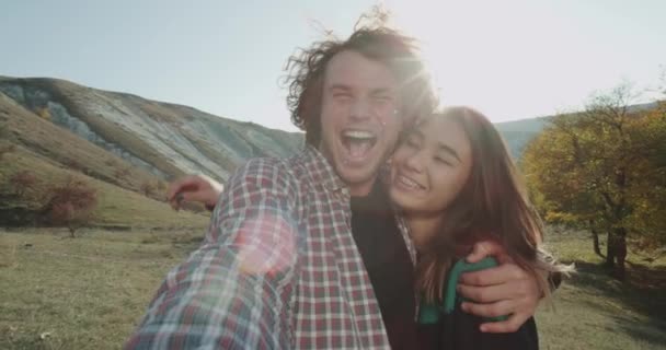 Krásný multikulturní pár dobře bavte společně v přírodě, se převzetí video selfie fotoaparátem, usmíval se a dělat ksichty. — Stock video