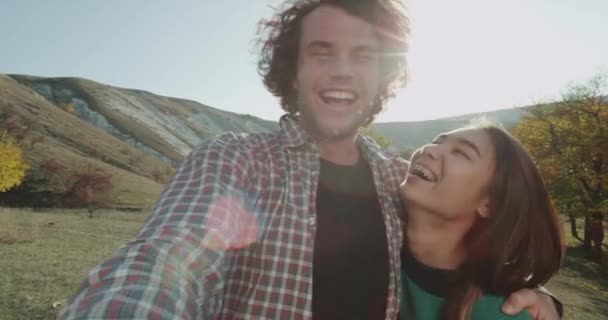 Χαμογελώντας νεαρό ζευγάρι μπροστά από την κάμερα, κρατώντας με το ένα χέρι και τη λήψη βίντεο για αναμνήσεις μέσα στη φύση. 4k — Αρχείο Βίντεο