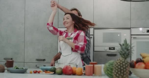 Moderne graue Küche charismatisches Paar, das vor der Kamera tanzt, während es das Essen zubereitet. — Stockvideo