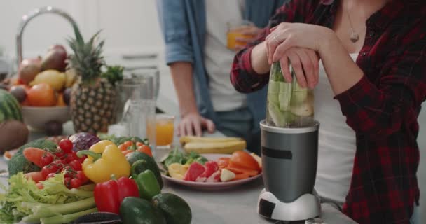 Grappige dame voor de camera springen onder het keukeneiland en beginnen te dacing tijdens het koken van het voedsel, de moderne keuken leuke sfeer volle tafel met groenten en fruit. — Stockvideo