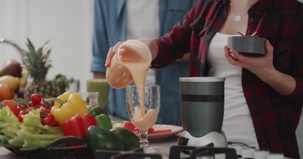 Mulher derramando o smoothie laranja em um copo grande, café da manhã saudável em um design de cozinha modem, casal juntos de manhã passar um tempo para preparar a comida . — Vídeo de Stock