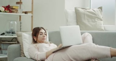 Bir kadın kanepede dizüstü bilgisayar, sabah rahat tasarım üzerinde pijama.