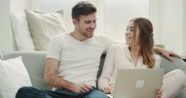 Bir çift kanepede oturan ve rahat tarzı şaşırtıcı notebook üzerinde bir şey sabah pijamayla.