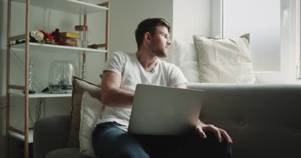 Uomo in pigiama al mattino che lavora sul suo taccuino bevendo caffè in salotto sul divano, design moderno . — Video Stock