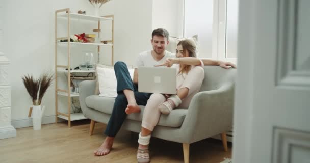 En la moderna pareja de la sala de estar utilizando un ordenador portátil pedir algo y el uso de un teléfono para hacer la confirmación de la orden . — Vídeos de Stock