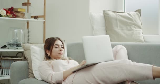 Eine Frau im Schlafanzug auf dem Sofa, am Laptop arbeitend, am Morgen gemütliches Design. — Stockvideo