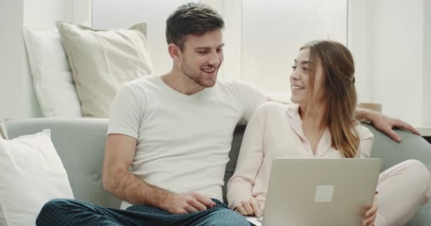 No pijama um casal de manhã sentado no sofá e assistindo a algo no notebook incrível estilo acolhedor . — Vídeo de Stock
