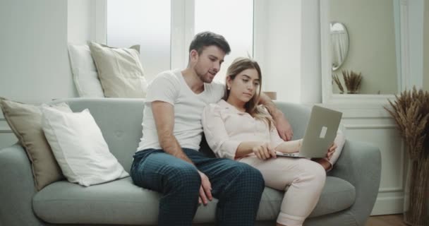 Харизматичная пара по утрам в живом диване смотрит что-то на блокноте счастливо проводя прекрасное время, оба в пижаме. 4k — стоковое видео