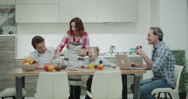 Schöne reife Familie am Morgen ein gemeinsames Frühstück am großen Tisch Mutter glücklich bereiten den Teller mit Müsli und Milch für ihre beiden Kinder, Vater sitzt auf dem Stuhl und schaut auf seine — Stockvideo