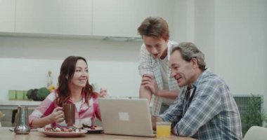 Olgun ailesine bir şey şaşırtıcı tasarım ile mutfakta yemek masasında dizüstü bilgisayar, yeni teknoloji kullanmak nasıl açıklamak karizmatik genç çocuk.