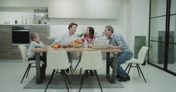 モダンなキッチンに成熟した家族の支出の時間彼らの夕食をとりながら一緒には ラップトップ上で何かを見て 素晴らしい時間を過ごす — ストック動画