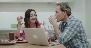 Birlikte birlikte güzel vakit, birbirlerini öpmeye kahvaltı alarak sabah çekici Olgun çift, onlar kendi mutfak masasının üzerinde bir dizüstü bilgisayar var.