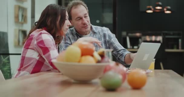 Ao tomar o café da manhã e beber café casal maduro na cozinha analisando algo do laptop pela manhã. 4k — Vídeo de Stock