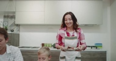 Olgun kadın sabahı onu aile üyeleri için o zaman mutlu yemek getirecek gıda yemek masası ve mutlu Kahvaltı almaya başlayan üzerinde hep birlikte.
