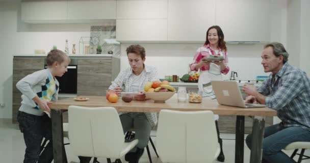 Dos chicos desayunan juntos con sus padres maduros en un diseño de cocina moderno, felices de pasar un buen rato juntos, familia moderna . — Vídeos de Stock