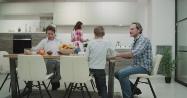 Matin dans une cuisine moderne famille attrayante prendre le petit déjeuner ensemble maman préparer la table avec délicieux papa alimentaire vérifier son e-mail à l'aide d'un ordinateur portable . — Video