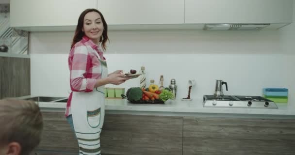 En un diseño de cocina increíble madre madura tomando el desayuno de la cocina y trae a sus hijos en la mesa de la cena estado de ánimo feliz y caras sonrientes para todos los miembros de la familia. 4k — Vídeos de Stock