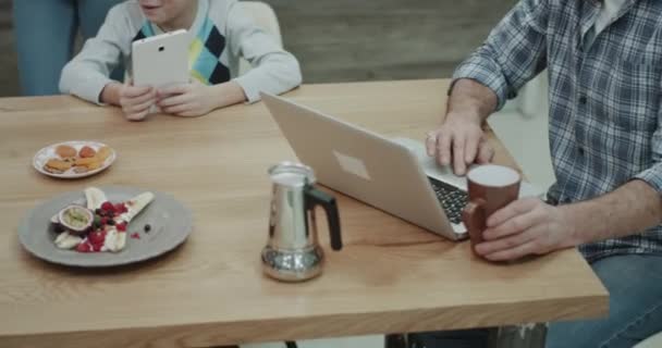 V čeledi ráno při snídani spolu táta jeho e‑mailů na přenosném počítači, matka dává její dva chlapci oběd box pro školy, děti tráví čas na tabletu. — Stock video