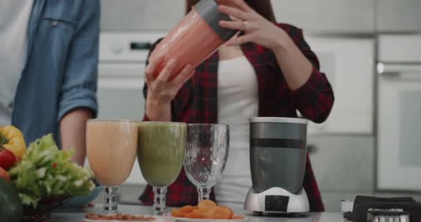 Молодая веганская пара делает смузи для всей семьи утром женщина наливает смузи в большой стакан, в современном дизайне кухни . — стоковое видео