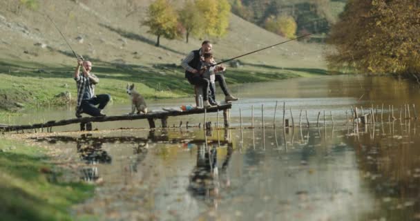 Deux amis, au milieu de la pêche en montagne dans un petit lac, un petit garçon mignon debout à côté de son père, un chien husky mignon se promenant . — Video