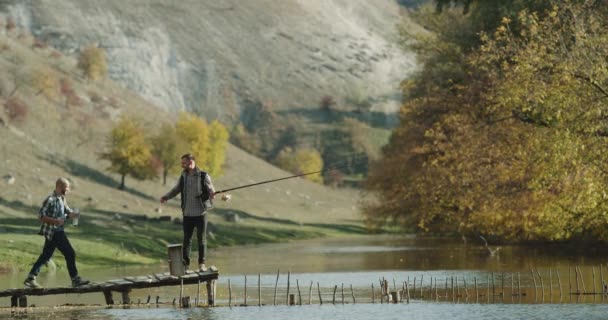 Due amici si incontrano oltre ad un bellissimo lago prima di iniziare a pescare bevono qualche bottiglia d'acqua e in una perfetta serata autunnale . — Video Stock