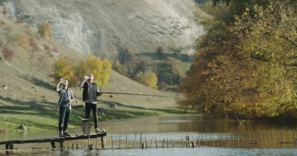 Boire des bouteilles d'eau deux gars à la nature jusqu'à attendre d'attraper des poissons du lac . — Video