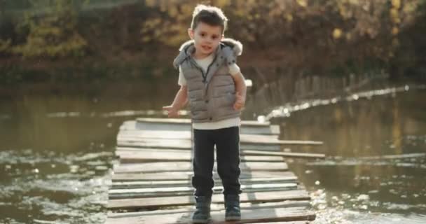 Харизматичний хлопчик перед камерою на природі біля озера рухається смішно . — стокове відео