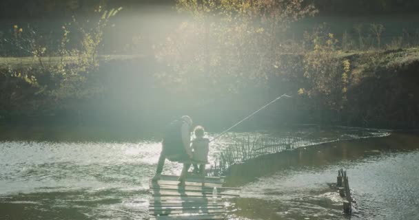 Незабываемые моменты папа и его маленький сын рыбачат на озере, сидя на стульях на мосту . — стоковое видео