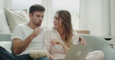 Karizmatik çift birlikte patlamış mısır yemek ve laptop bir şey hafta sonu harcama.